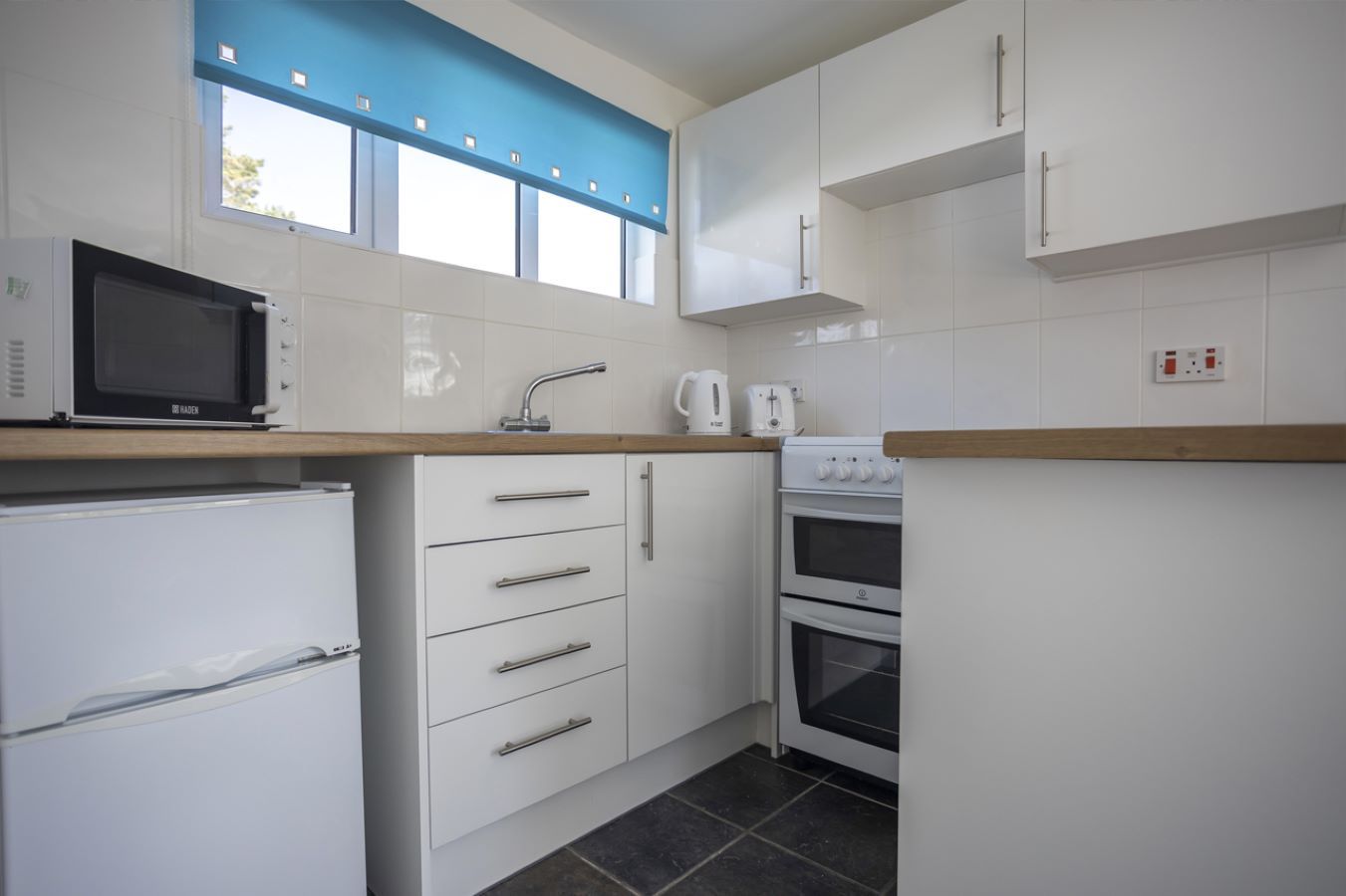 A compact kitchen with white cabinets, a microwave, a kettle, a toaster, and a stove.