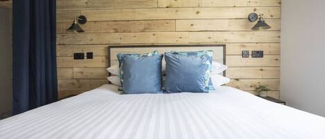 Un letto con una coperta a righe bianche, due cuscini blu e una testiera in legno.