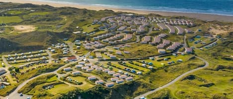 An aerial view of a coastal caravan park with rows of caravans and mobile homes, surrounded by greenery and a beach.