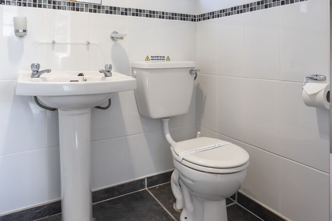 Un baño con lavamanos blanco, inodoro y paredes con azulejos.