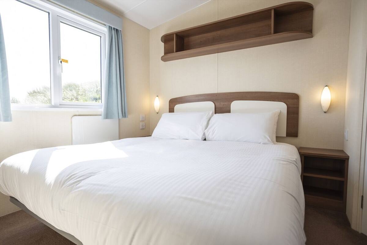 A hotel room with a large bed, wooden headboard, bedside tables, and a window with curtains.