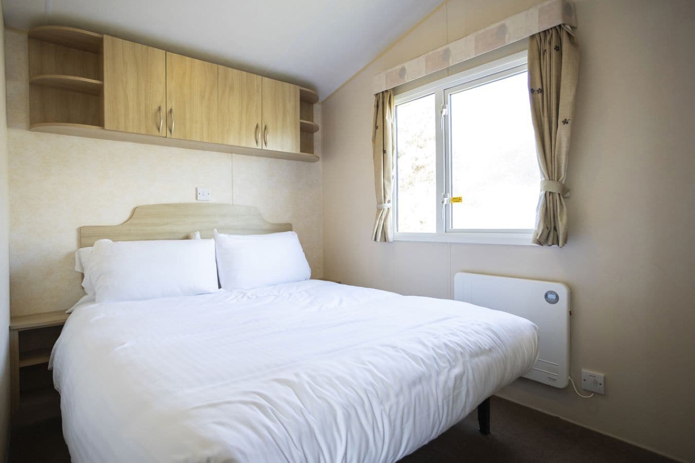 Een slaapkamer met een bed, een houten kledingkast, een raam met gordijnen en een radiator.