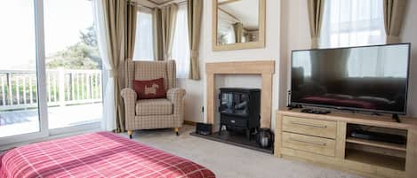 A bedroom with a bed, a TV, a fireplace, a chair, and a balcony.