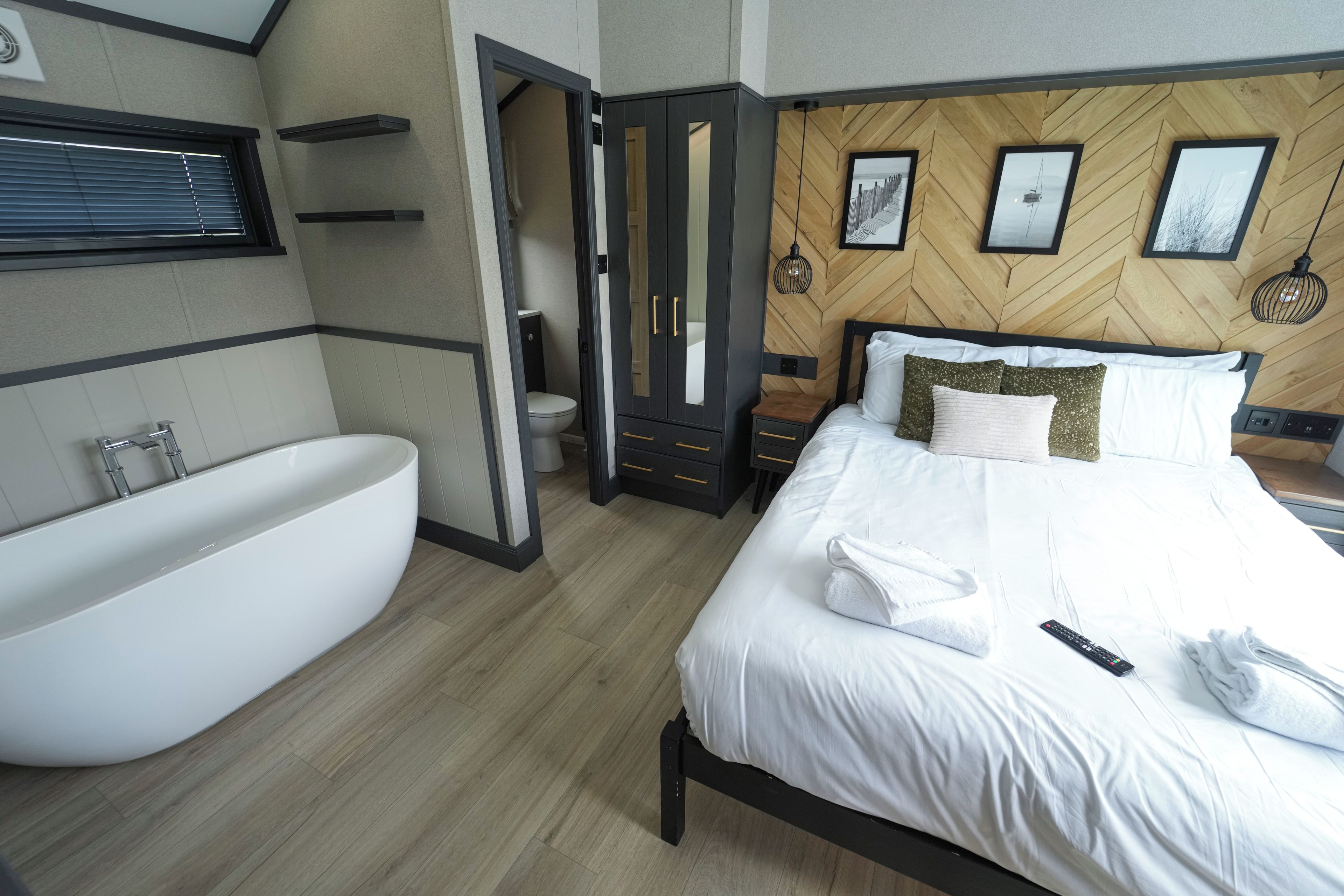 A modern bedroom with a large bed, a built-in bathtub, and a wooden herringbone wall pattern.