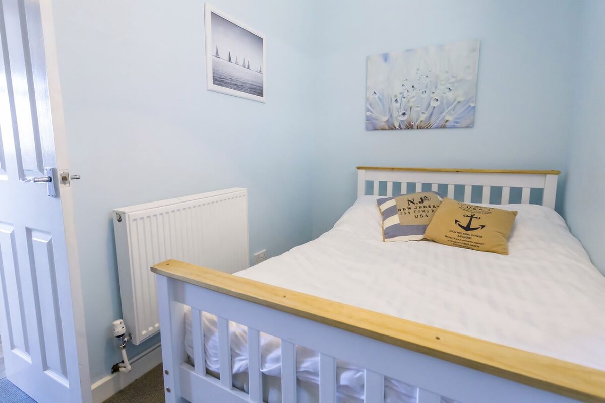 A bedroom with a single bed, a white radiator, a door, and a wall with two framed pictures.