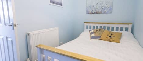 A bedroom with a single bed, a white radiator, a door, and a wall with two framed pictures.