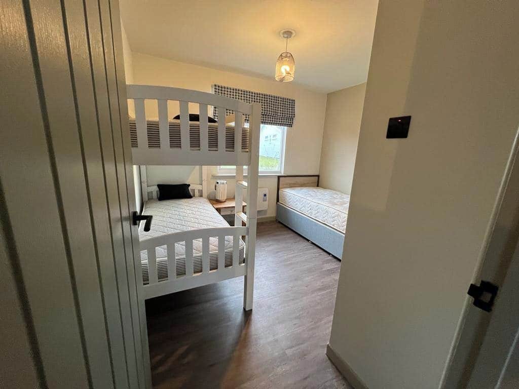 Una camera da letto con un letto a castello, un letto singolo, una finestra vista e un comodino con una lampada.
