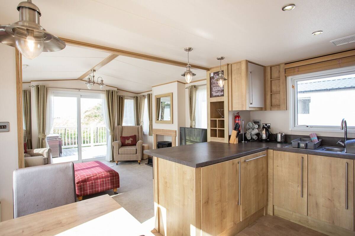 A compact kitchen with wooden cabinets, a dining area with a red checkered tablecloth, and a view of a balcony with outdoor furniture.