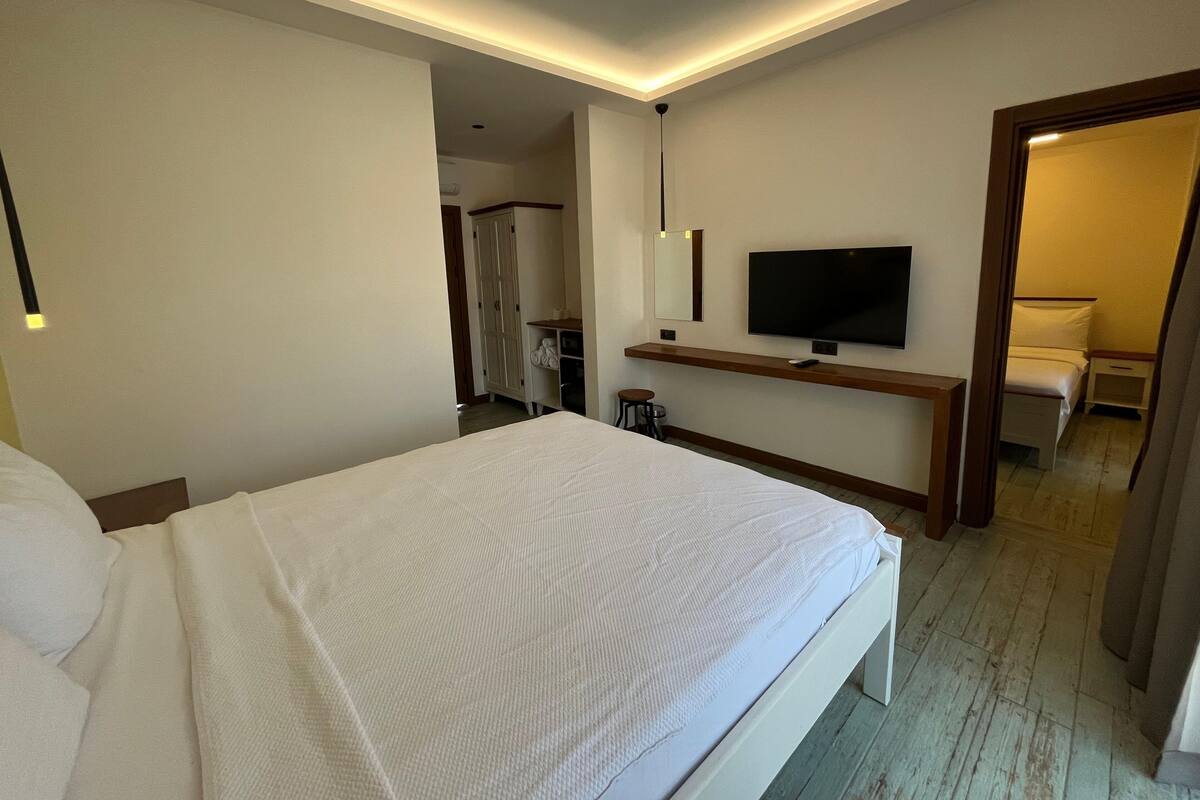 A hotel room with a large bed, a TV mounted on the wall, a desk with a chair, and a wardrobe.