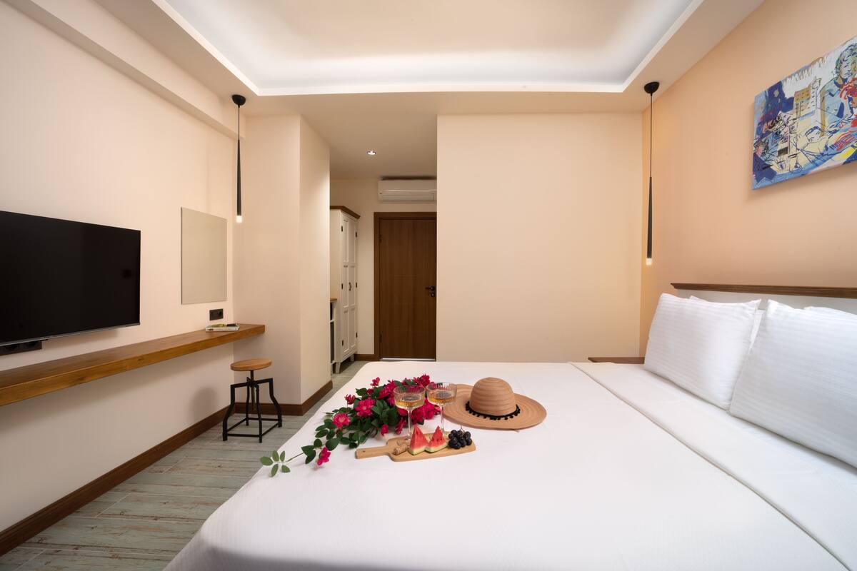 A hotel room with a bed, a TV, a wooden shelf, a desk, and a painting on the wall.