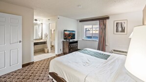 Une chambre d’hôtel avec un grand lit, une télévision, une salle de bain avec un miroir et une fenêtre avec des rideaux.