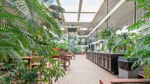 Un vaste espace intérieur à plusieurs niveaux, comprenant un espace central ouvert entouré de tables et de chaises, ainsi que diverses plantes en pot.