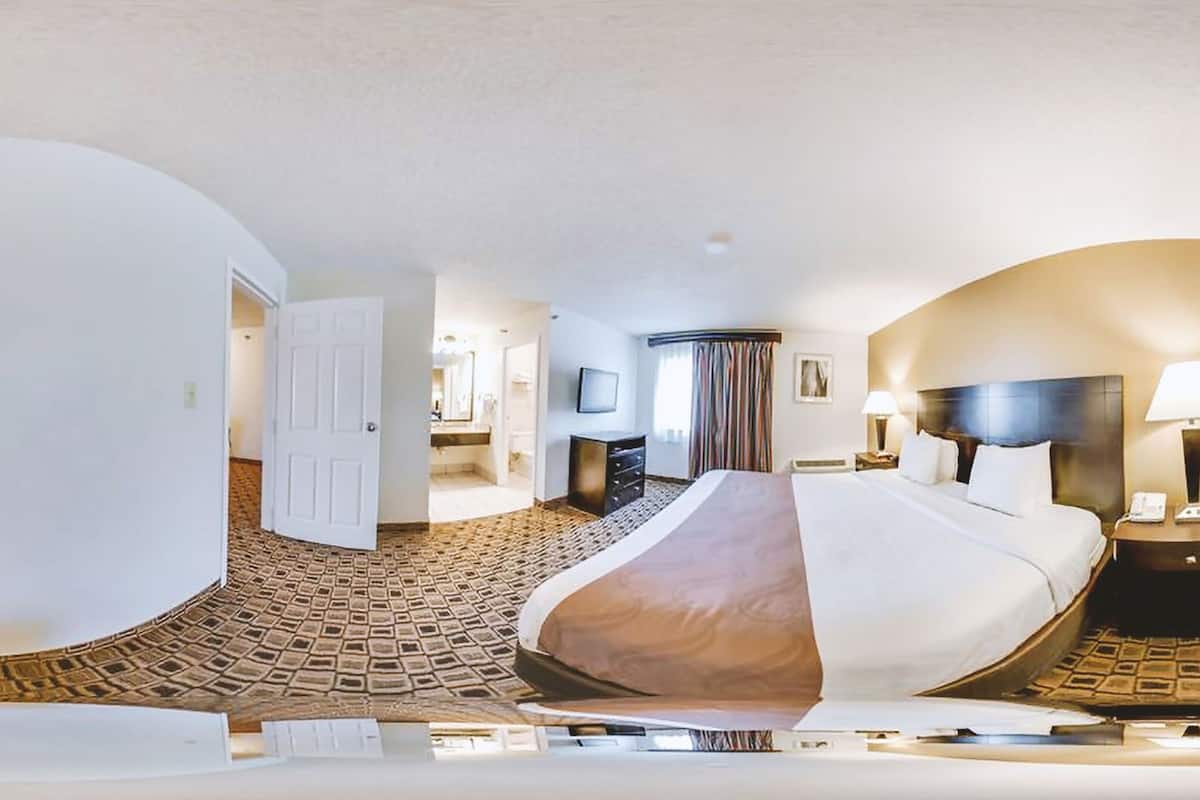 Una habitación de hotel con una cama grande, un escritorio, una silla, un televisor y un baño visible a través de una puerta abierta.