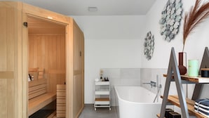 Une salle de bain moderne avec une baignoire sur pieds, des étagères en bois et un espace sauna.
