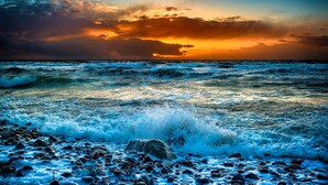 Une plage où les vagues s’écrasent contre les rochers, avec un coucher de soleil en arrière-plan.