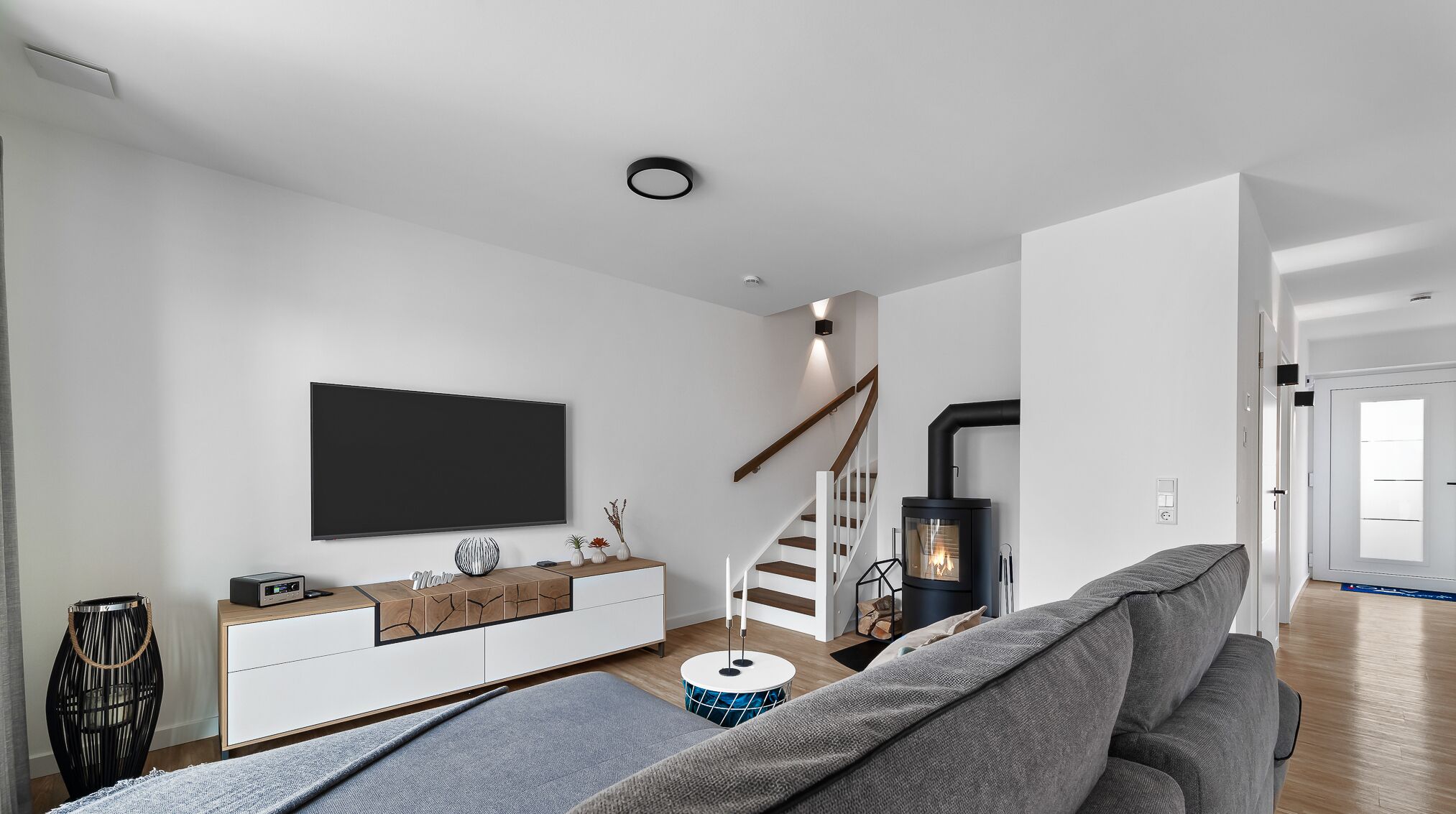 A modern living room with a flat-screen TV, a fireplace, a staircase, and a sofa.
