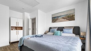 A modern bedroom with a bed, a wardrobe, a painting, and a nightstand.