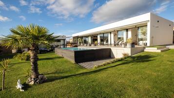 Une maison moderne dotée d’une piscine, d’un patio couvert et d’une pelouse bien entretenue.