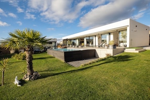 Une maison moderne dotée d’une piscine, d’un patio couvert et d’une pelouse bien entretenue.