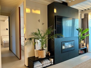 Un salon moderne avec un meuble de rangement noir pour les appareils électroniques, un grand téléviseur à écran plat et une plante en pot.