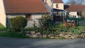 A two-story house with a red-tiled roof and a small garden area with a table and chairs. - Our quirky Gite is 4 minutes drive to Gouzon and 12 minutes drive to Boussac. (Trois Fomds)