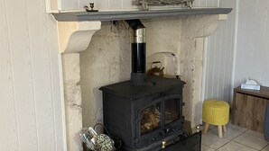 A cozy room with a wood-burning stove, a woven basket, and a small stool. - Our quirky Gite is 4 minutes drive to Gouzon and 12 minutes drive to Boussac. (Trois Fomds)