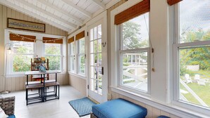 A sunroom with large windows, a wooden table, and a blue bench. - Beachwood Cottage by Bayley Vacation Rentals (Scarborough)