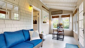 A cozy room with a blue sofa, a small table, and a window with a view of greenery. - Beachwood Cottage by Bayley Vacation Rentals (Scarborough)
