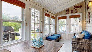 A sunroom with large windows, a wooden table, a blue decorative piece, a wicker sofa, and a sign that reads "SEA". - Beachwood Cottage by Bayley Vacation Rentals (Scarborough)
