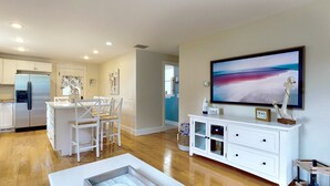 A modern kitchen with white cabinets, a stainless steel refrigerator, and a dining area with white chairs. - Beachwood Cottage by Bayley Vacation Rentals (Scarborough)