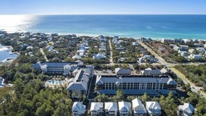 An aerial view of a coastal residential area with houses, a large building with a swimming pool, and the ocean in the background.