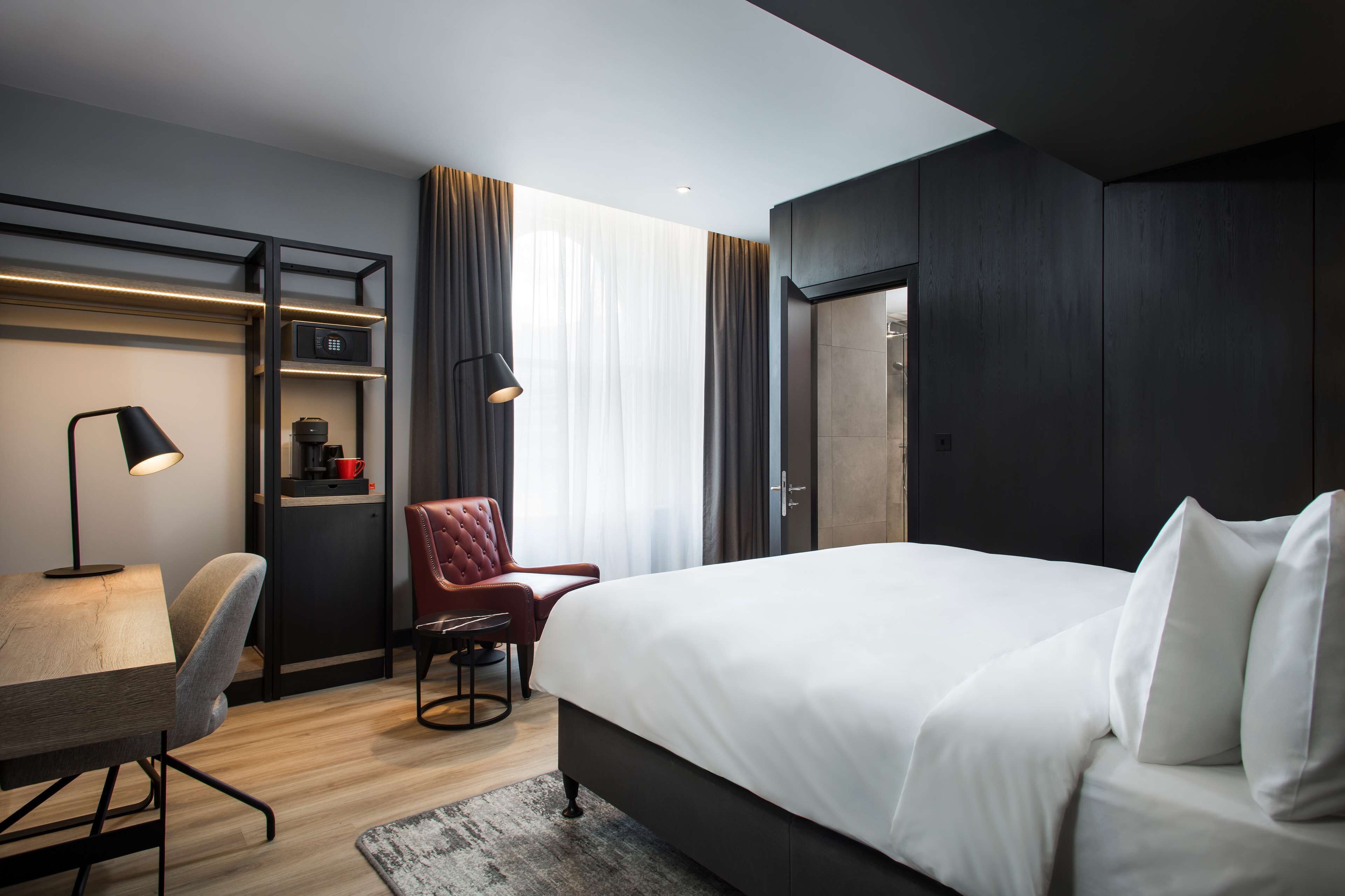 Una habitación de hotel moderna con una cama grande, un escritorio, una silla y un armario.