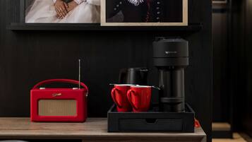 A framed portrait of a person in historical attire, a coffee maker, and red cups on a wooden table.