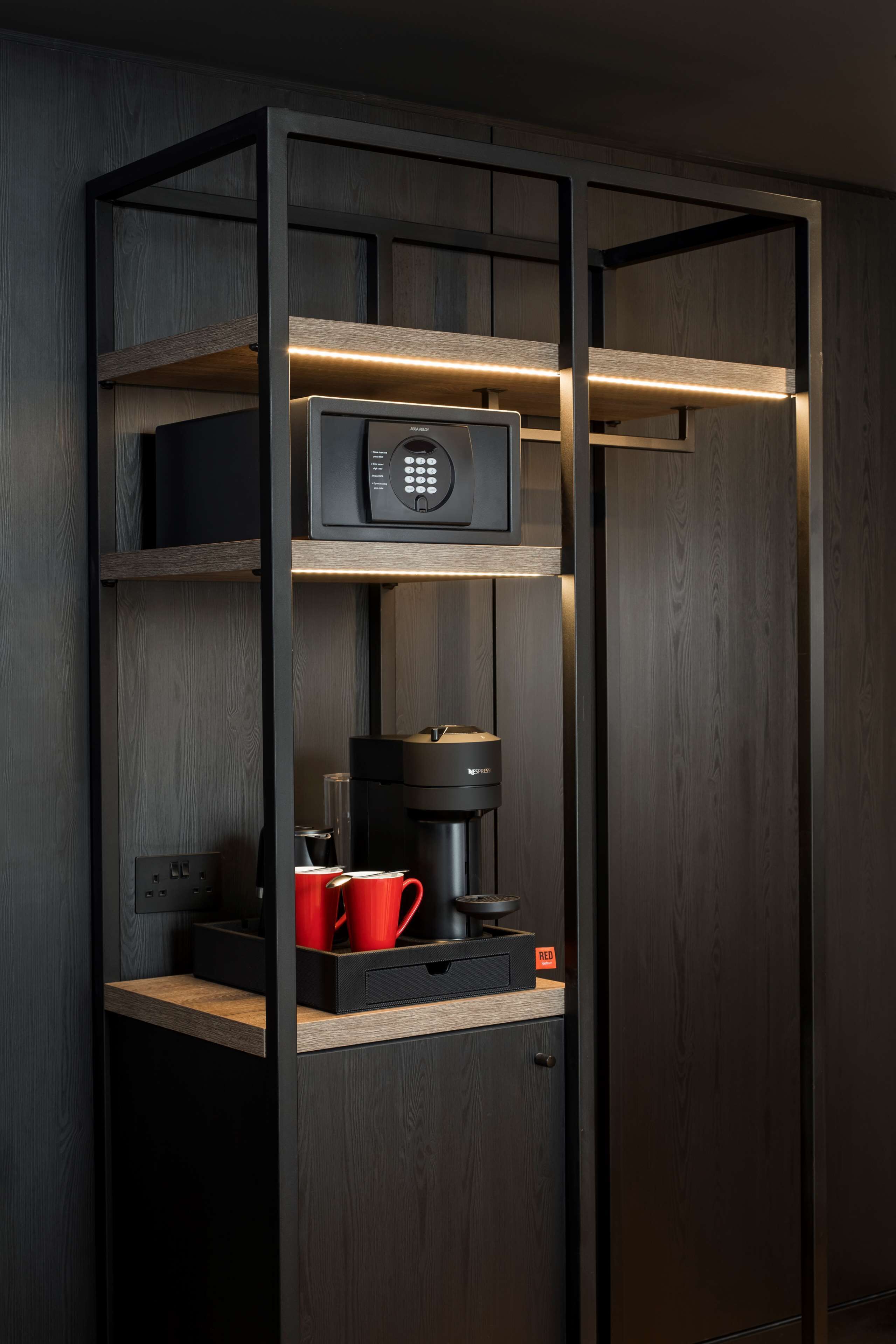 Una cucina moderna con forno a microonde integrato, macchina da caffè e tazza rossa su uno scaffale in legno.