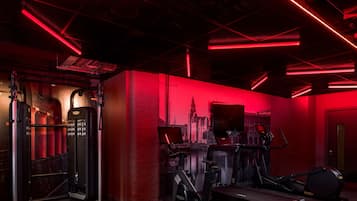 A gym with red lighting, exercise equipment, and a cityscape mural on the wall.