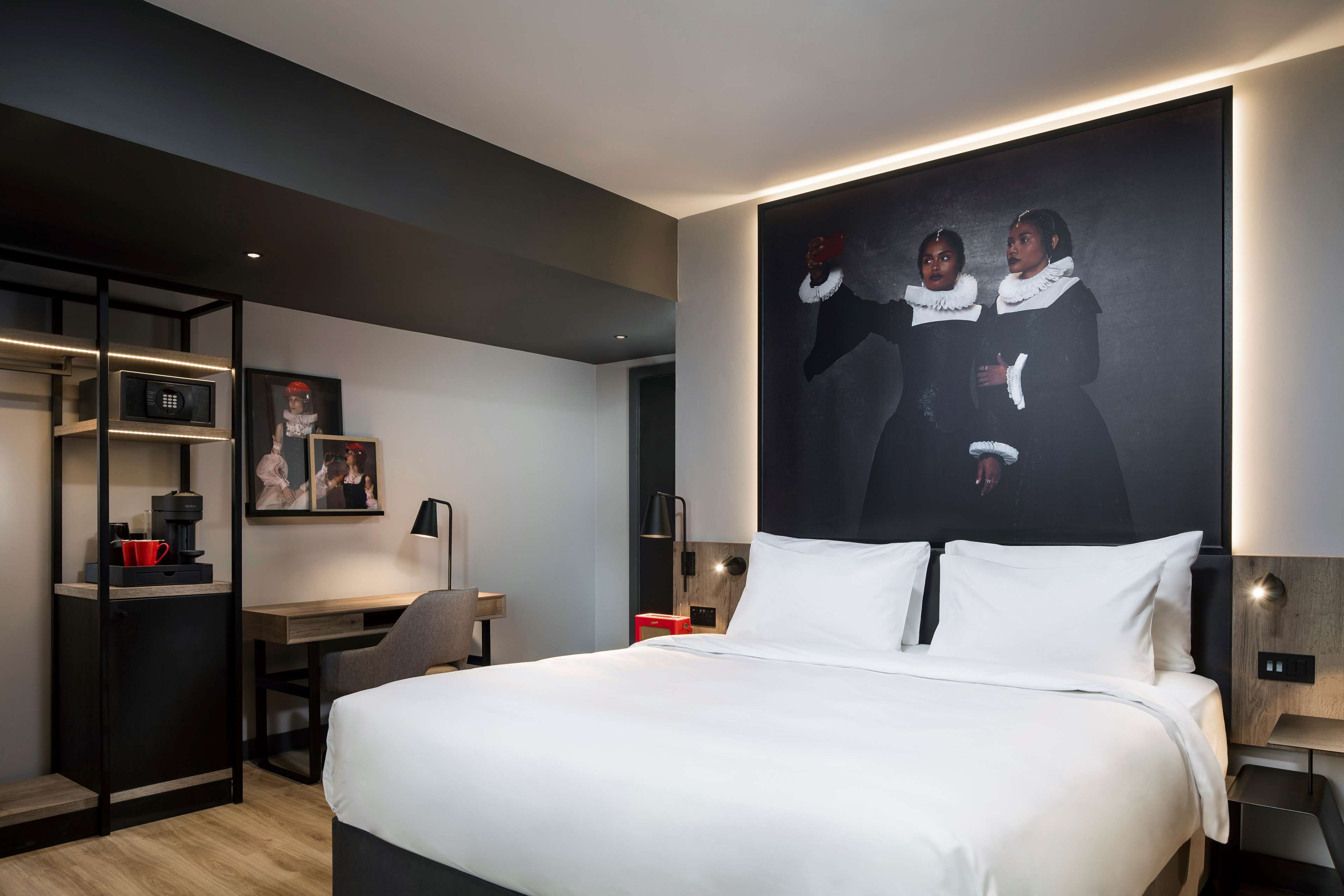A modern hotel room with a large bed, a desk, a microwave, and a coffee machine.