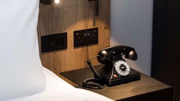 A wooden bedside table with a black rotary phone and a wall-mounted light fixture.
