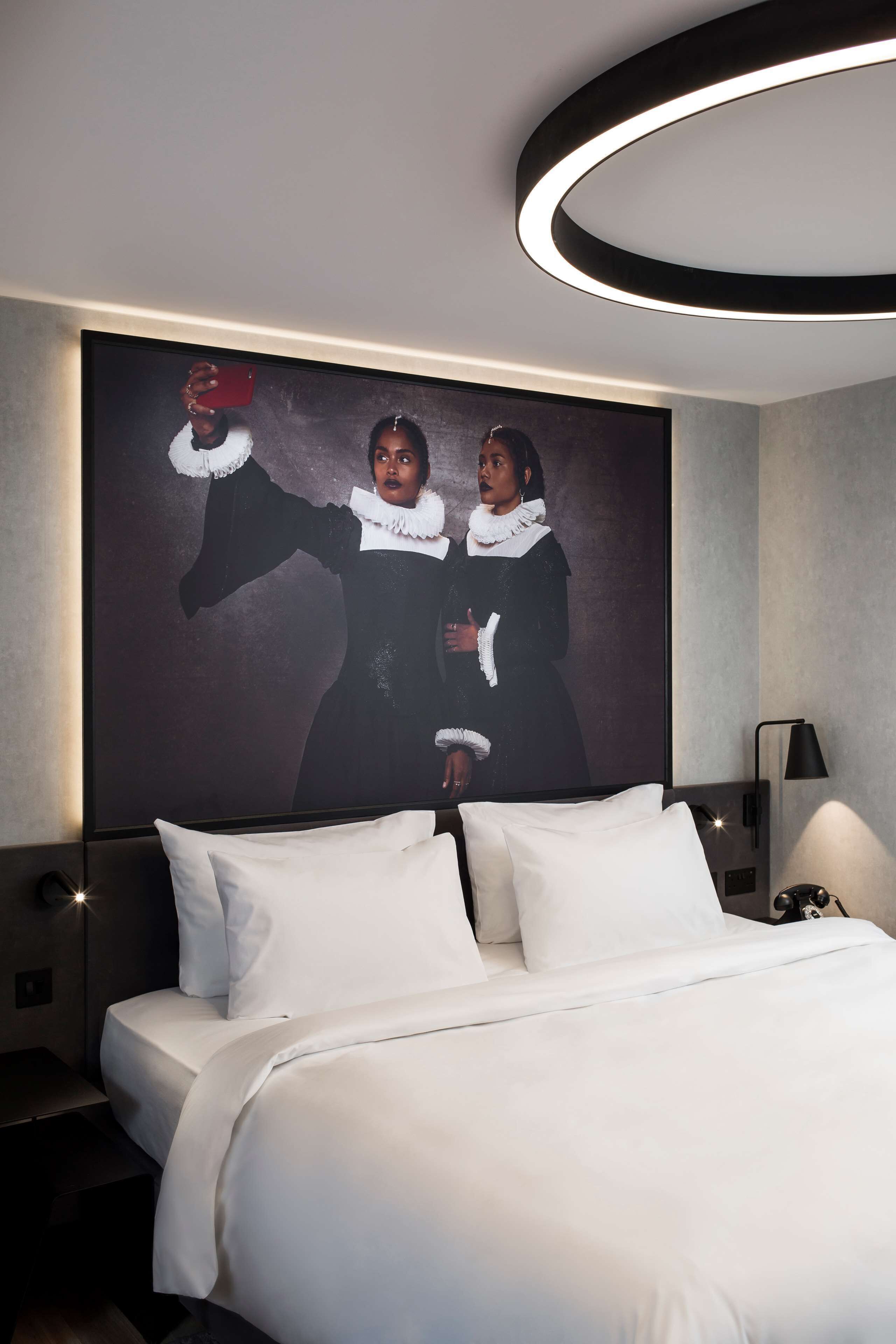 Habitación de hotel moderna con una cama grande, una obra de arte enmarcada en la pared y un aplique circular sobre la cama.