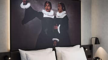 Habitación de hotel moderna con una cama grande, una obra de arte enmarcada en la pared y un aplique circular sobre la cama.