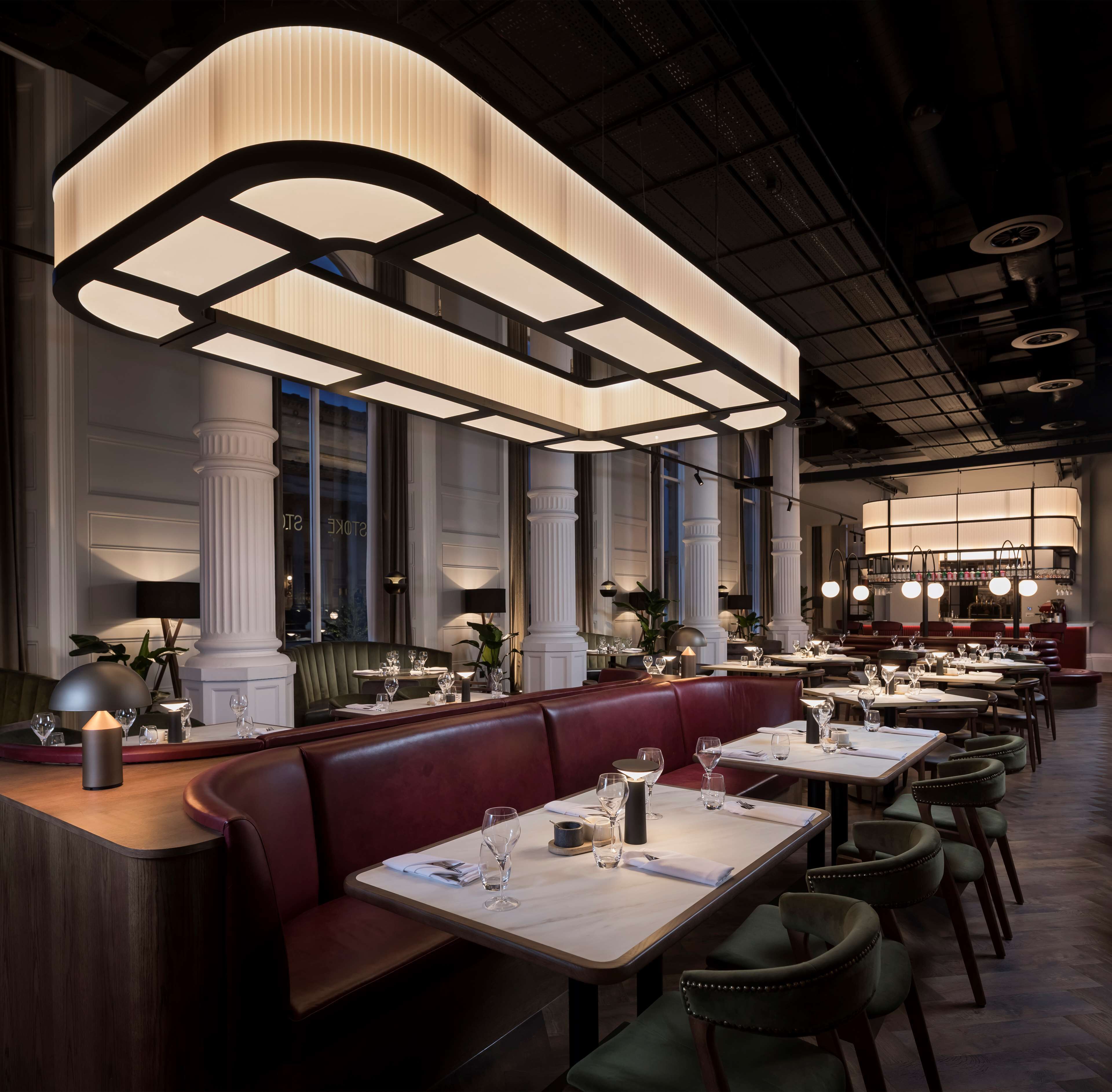 A restaurant interior with high ceilings, large windows, and a mix of seating including booths and tables.
