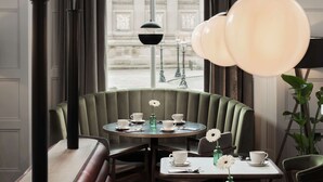 A restaurant with a green booth seating area, round tables with white tableware, and a view of a classical building through large windows. - Radisson RED Liverpool (Liverpool)