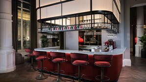 A bar area with a curved counter, red bar stools, and a variety of bottles and glasses on shelves. - Radisson RED Liverpool (Liverpool)
