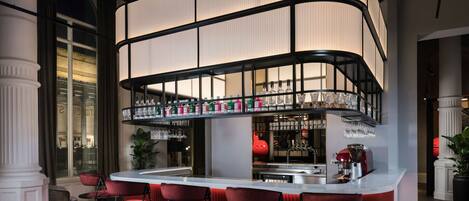 A bar area with a curved counter, red bar stools, and a variety of bottles and glasses on shelves.