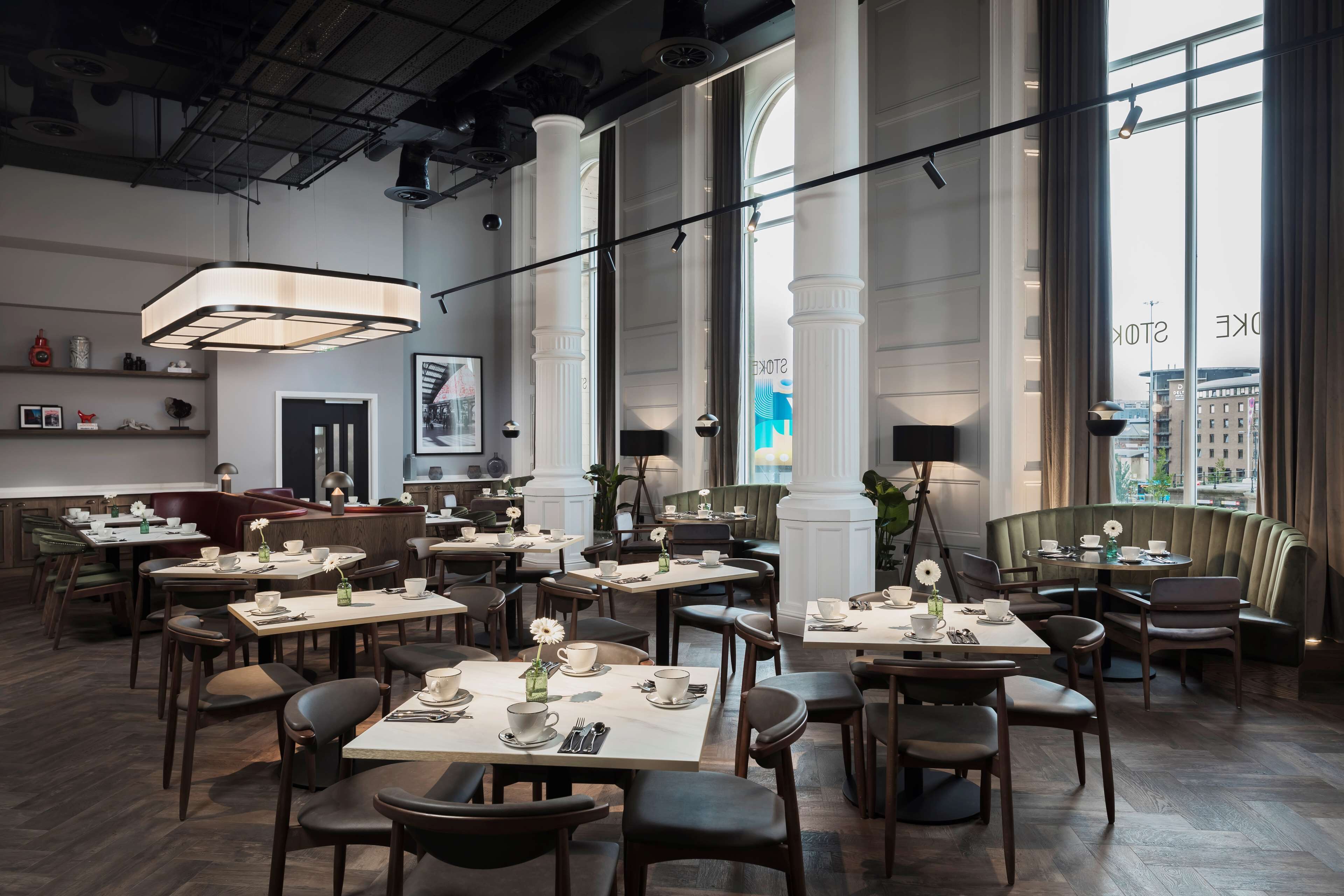 A modern restaurant with high ceilings, large windows, and a mix of seating options including tables and booths.