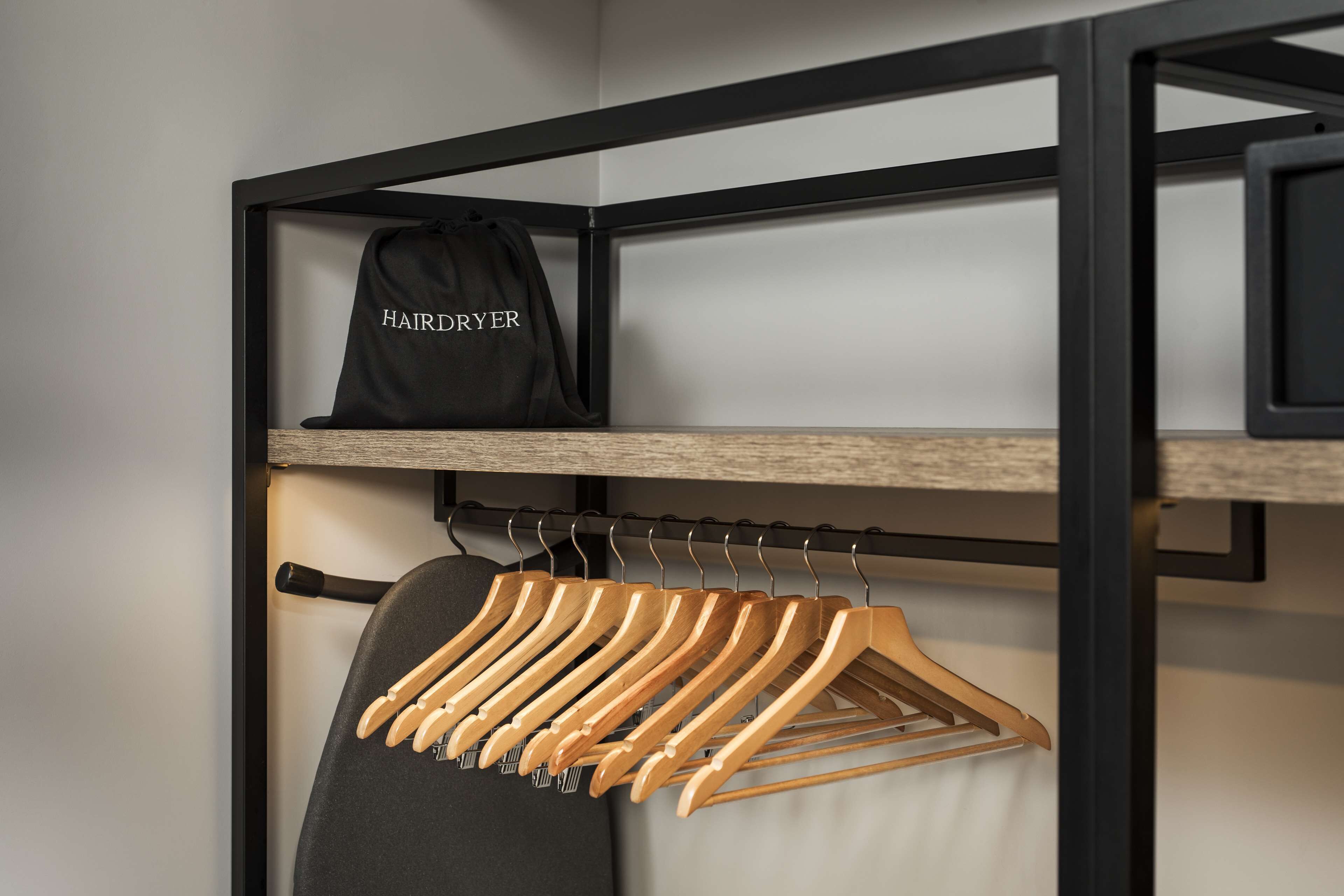 A clothing rack with hangers and a black bag labeled "HAIRDRYER" on a shelf.