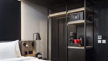 Una habitación de hotel moderna con una cama, una mesita de noche con teléfono, un escritorio con cafetera y una taza roja, y un microondas incorporado.