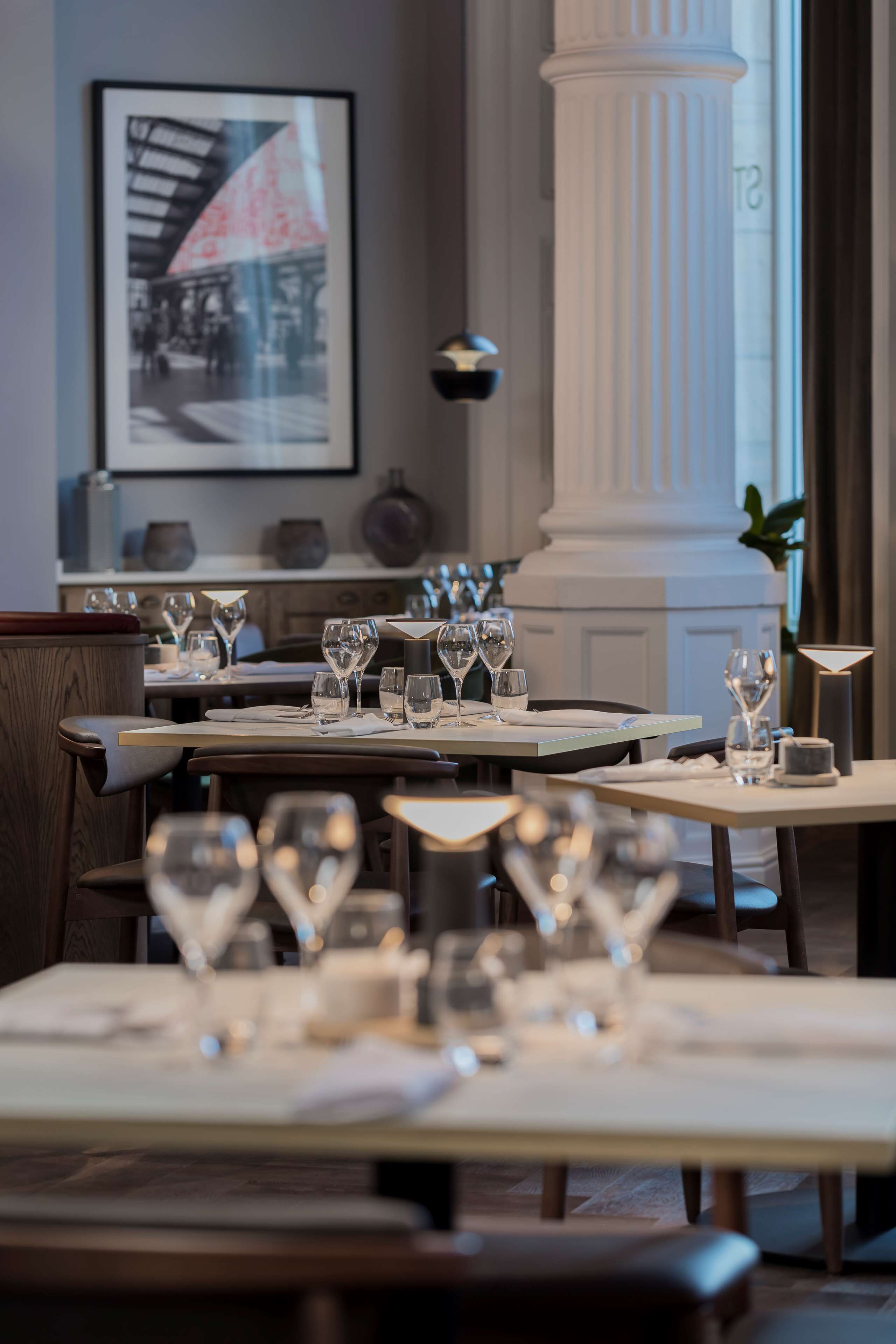 A restaurant interior with tables set for dining, a large column, and a framed picture on the wall.