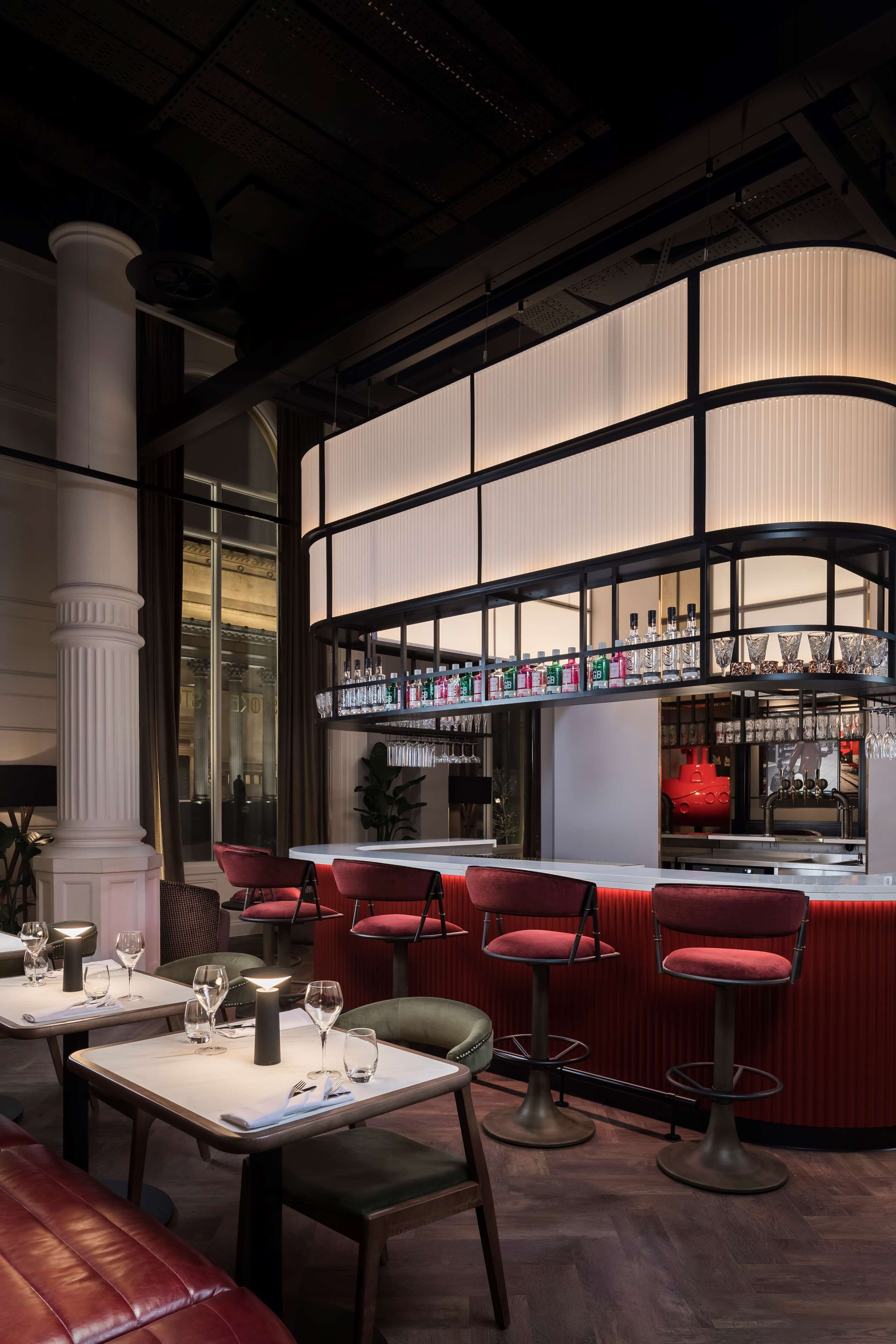 A bar area with red bar stools, a white countertop, and shelves stocked with bottles and glasses.