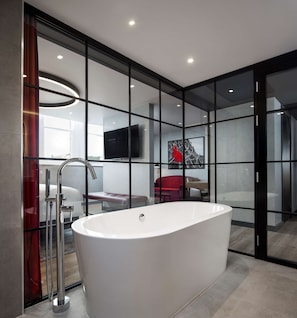 A modern bathroom with a freestanding bathtub, a glass shower enclosure, and a flat-screen TV mounted on the wall.