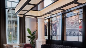 A modern lounge area with a curved ceiling, a black sofa, two pink armchairs, a small round table, and a red patterned rug. - Radisson RED Liverpool (Liverpool)